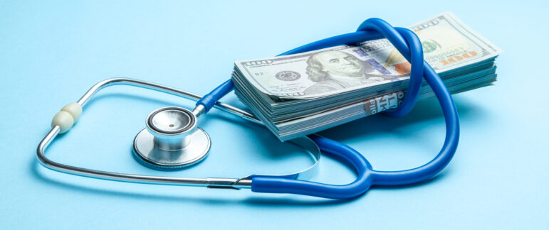 Stack of cash dollars and stethoscope on blue background. The co