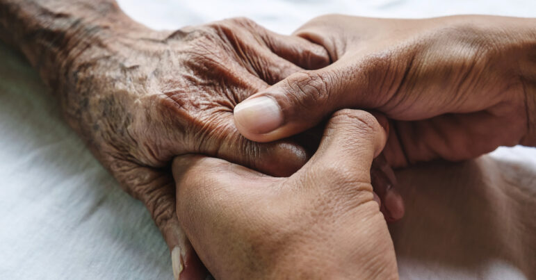 Hands of a younger man clasp the hands of an older man