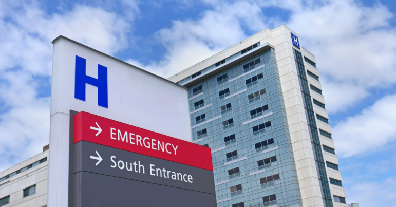 A sign directing patients where to enter the hospital. The hospital stands tall in the background.