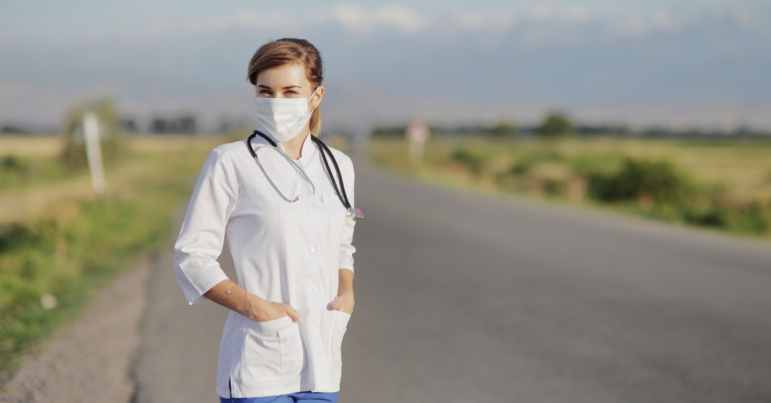 a rural doctor stands in a road with her mask on and a stethoscope around her neck